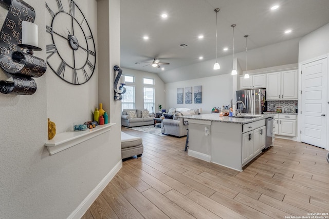 kitchen with a center island with sink, hanging light fixtures, light hardwood / wood-style flooring, appliances with stainless steel finishes, and white cabinetry