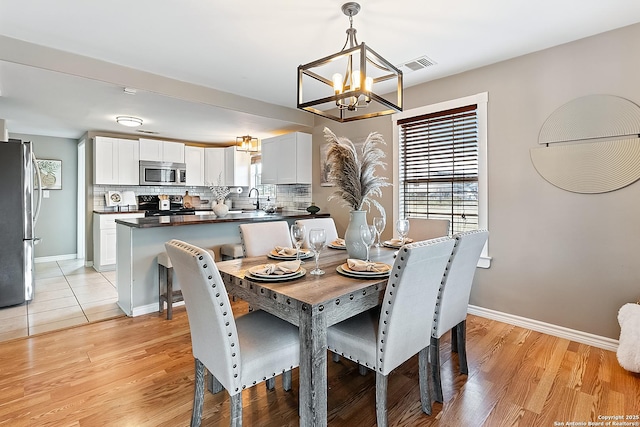 dining space with light wood-type flooring, an inviting chandelier, and sink