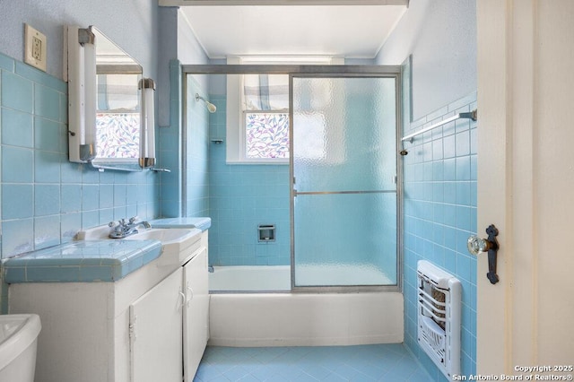 full bathroom featuring heating unit, tile walls, shower / bath combination with glass door, tile patterned flooring, and vanity