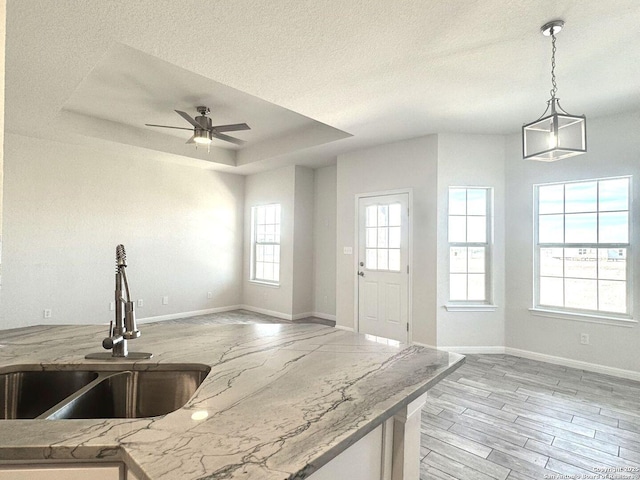 kitchen with ceiling fan, sink, a raised ceiling, a textured ceiling, and decorative light fixtures