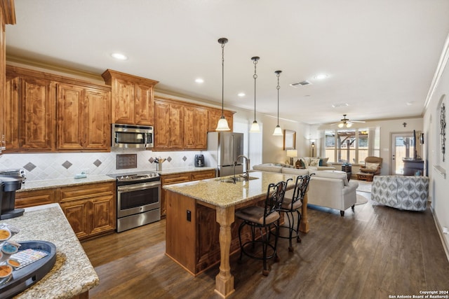 kitchen featuring pendant lighting, a center island with sink, crown molding, appliances with stainless steel finishes, and a breakfast bar area