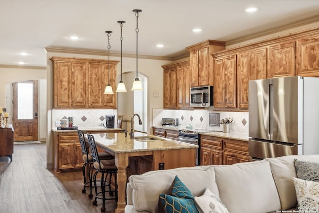 kitchen featuring sink, stainless steel appliances, backsplash, decorative light fixtures, and a center island with sink