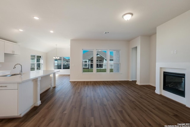 kitchen featuring vaulted ceiling, dark wood-type flooring, sink, white cabinetry, and hanging light fixtures