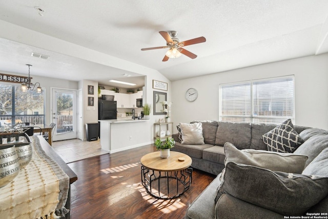 living room with plenty of natural light, vaulted ceiling, ceiling fan with notable chandelier, and dark wood-type flooring