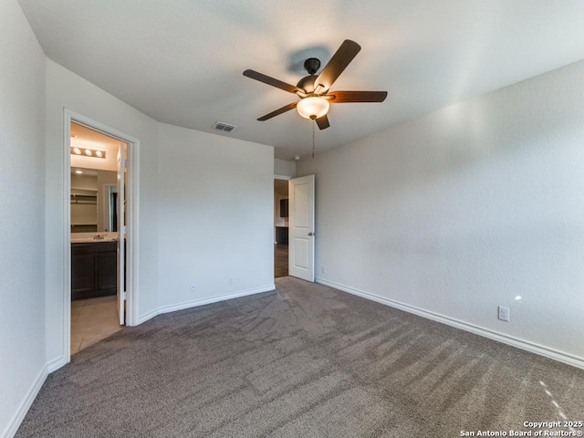 unfurnished bedroom featuring ceiling fan, ensuite bathroom, and dark carpet