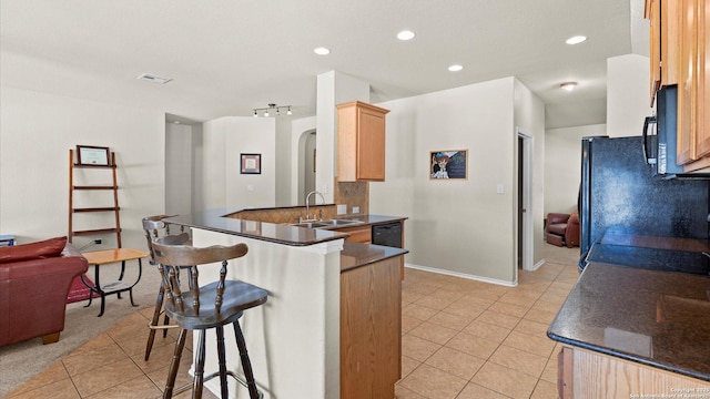 kitchen with light brown cabinets, black appliances, sink, kitchen peninsula, and a breakfast bar area