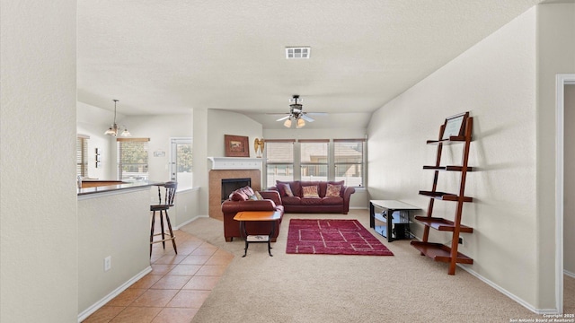 tiled living room with a tile fireplace, ceiling fan with notable chandelier, vaulted ceiling, and plenty of natural light