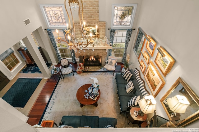 living room featuring hardwood / wood-style flooring, a brick fireplace, a high ceiling, and an inviting chandelier