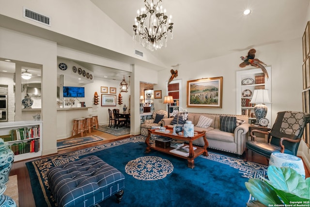 living room with built in shelves, hardwood / wood-style flooring, high vaulted ceiling, and a notable chandelier