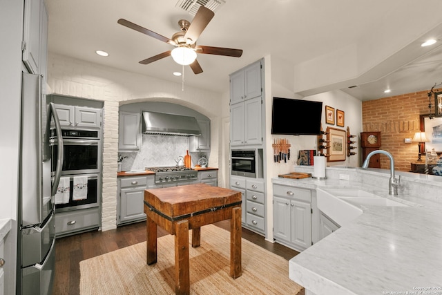 kitchen featuring backsplash, wall chimney exhaust hood, stainless steel appliances, sink, and gray cabinets