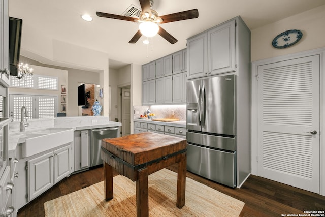 kitchen with gray cabinetry, ceiling fan with notable chandelier, sink, dark hardwood / wood-style flooring, and stainless steel appliances