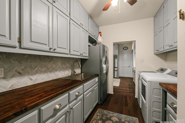 kitchen featuring dark wood-type flooring, wooden counters, sink, ceiling fan, and independent washer and dryer