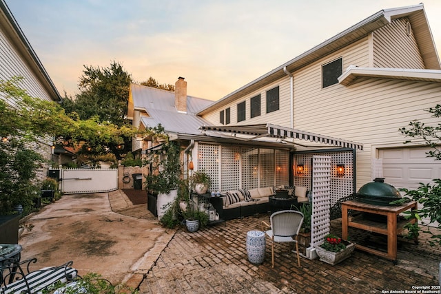 back house at dusk featuring outdoor lounge area, a patio, and a garage