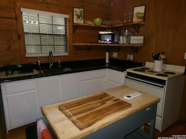 kitchen featuring white range with electric stovetop, sink, white cabinets, butcher block countertops, and wood walls