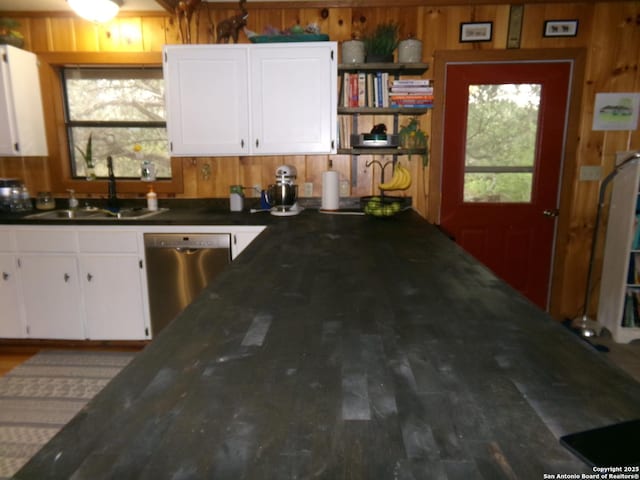 kitchen with white cabinetry, dishwasher, sink, wood walls, and dark stone counters