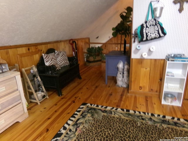 bedroom with a textured ceiling, wooden walls, wood-type flooring, and vaulted ceiling