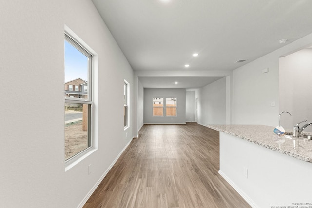 unfurnished living room featuring sink, a healthy amount of sunlight, and light hardwood / wood-style floors