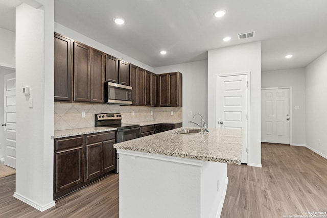 kitchen with dark brown cabinetry, sink, electric range oven, tasteful backsplash, and a kitchen island with sink