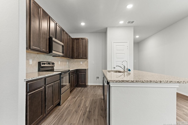 kitchen with hardwood / wood-style floors, backsplash, a kitchen island with sink, sink, and appliances with stainless steel finishes