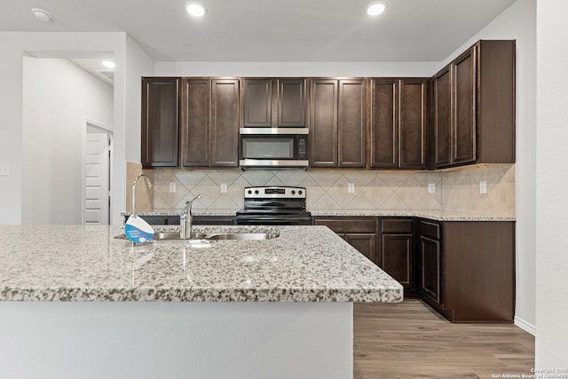 kitchen with stainless steel appliances, tasteful backsplash, light stone counters, dark brown cabinets, and light wood-type flooring