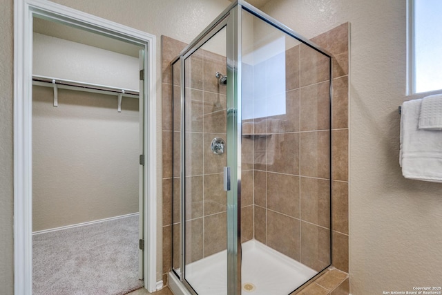 bathroom with a stall shower, a walk in closet, and a textured wall