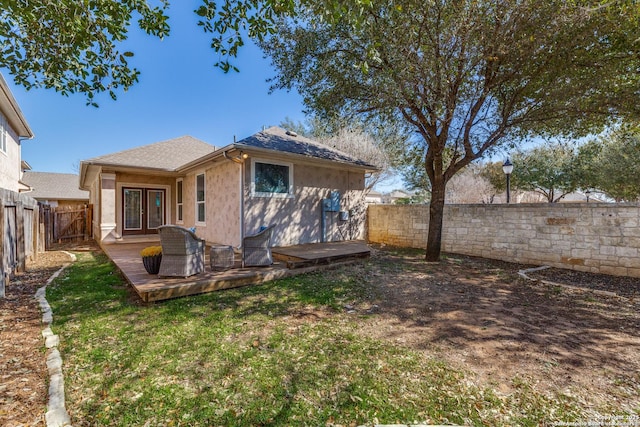 rear view of property with roof with shingles, a fenced backyard, french doors, a deck, and a lawn