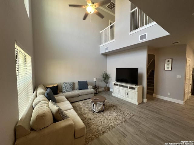 living room with ceiling fan, a high ceiling, and light hardwood / wood-style flooring