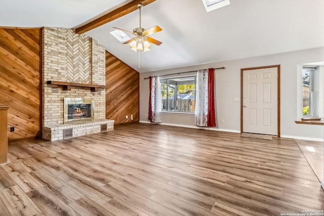 unfurnished living room featuring ceiling fan, wooden walls, light hardwood / wood-style flooring, a fireplace, and vaulted ceiling with beams