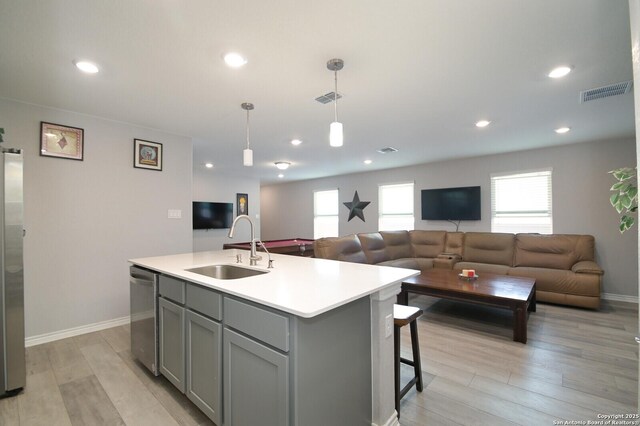 kitchen featuring sink, hanging light fixtures, light hardwood / wood-style floors, a center island with sink, and appliances with stainless steel finishes