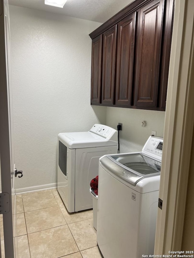 washroom featuring washing machine and dryer, cabinets, and light tile patterned floors