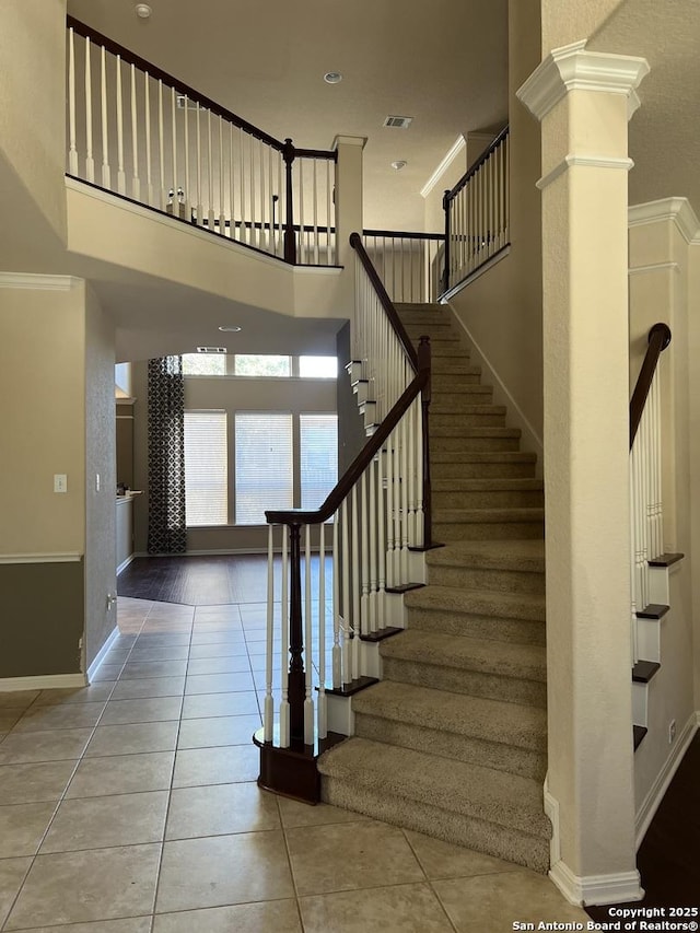 stairway featuring tile patterned flooring, ornamental molding, and decorative columns