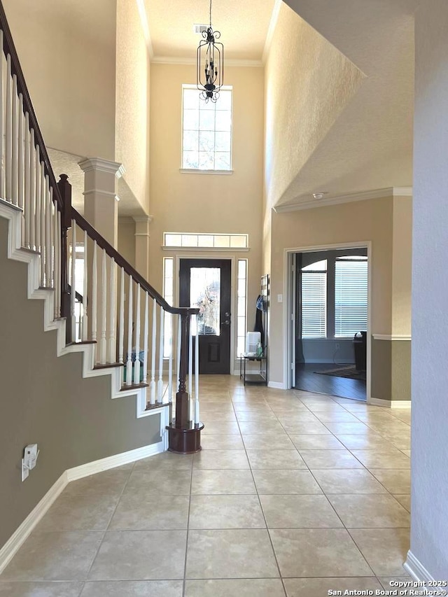 tiled foyer entrance with a wealth of natural light, a chandelier, crown molding, and a high ceiling