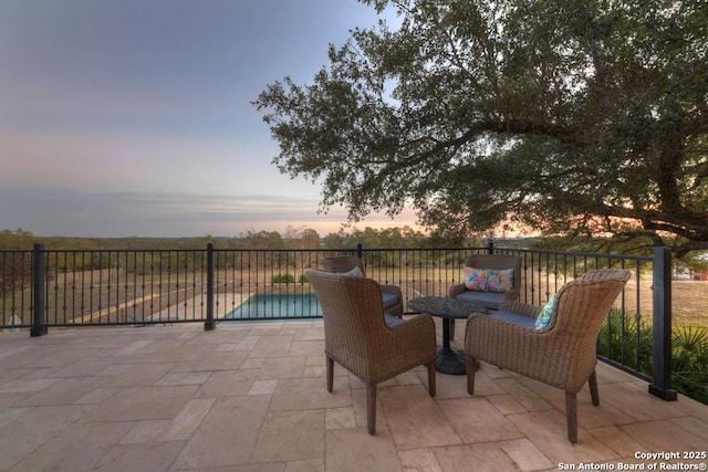 patio terrace at dusk featuring a fenced in pool