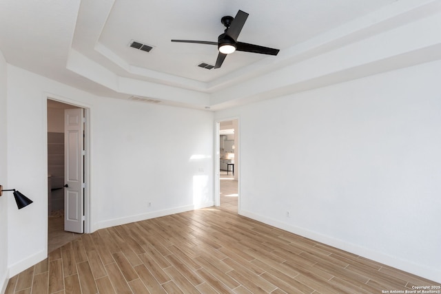 empty room with ceiling fan and a raised ceiling