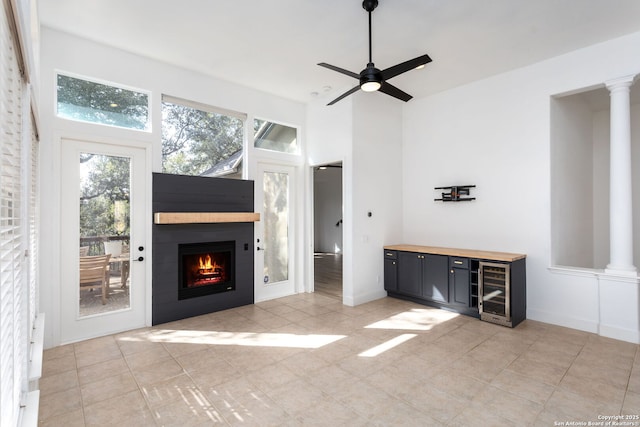 unfurnished living room with light tile patterned floors, ornate columns, ceiling fan, and beverage cooler