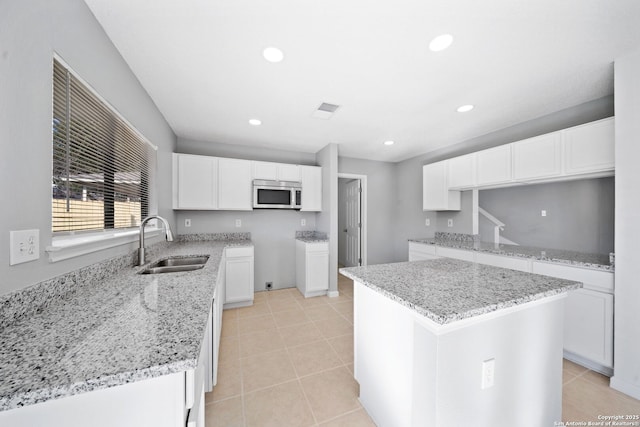 kitchen with light stone counters, sink, light tile patterned floors, white cabinets, and a kitchen island