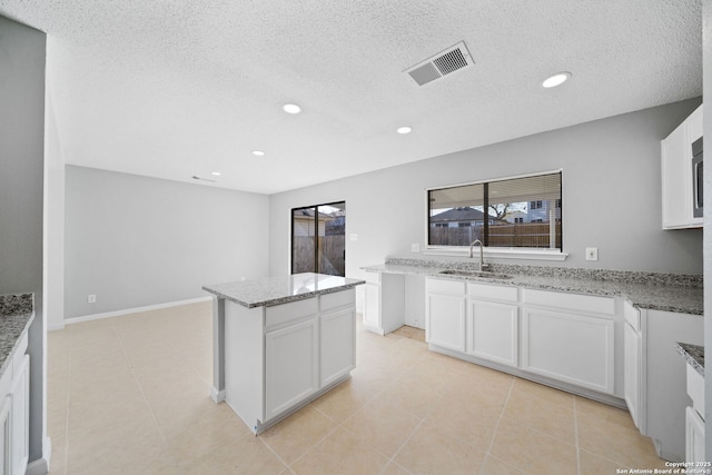 kitchen with light stone counters, a textured ceiling, sink, a center island, and white cabinetry