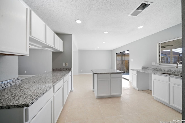 kitchen featuring white cabinetry, sink, a center island, light stone counters, and light tile patterned floors