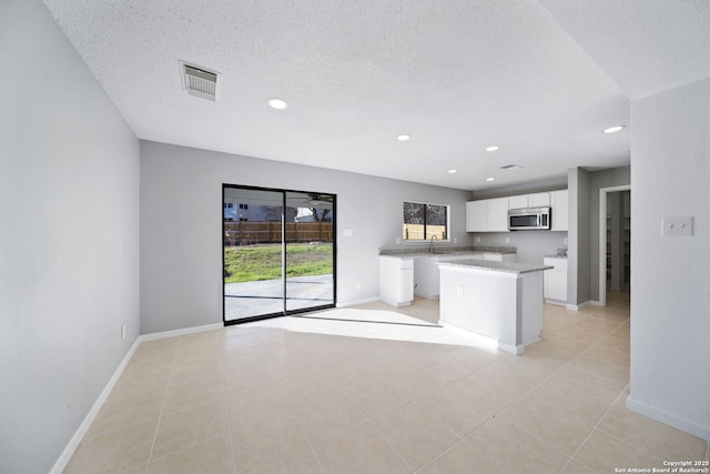 kitchen with a textured ceiling, sink, light tile patterned floors, white cabinets, and a center island