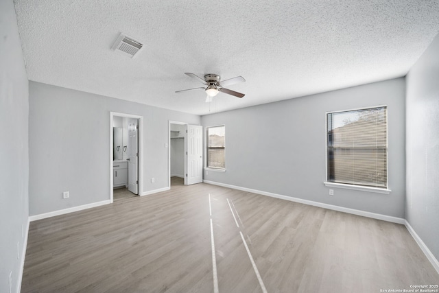 unfurnished bedroom with a walk in closet, ceiling fan, multiple windows, connected bathroom, and light hardwood / wood-style floors