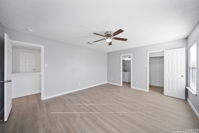 unfurnished bedroom featuring ensuite bath, ceiling fan, light hardwood / wood-style floors, a textured ceiling, and a walk in closet