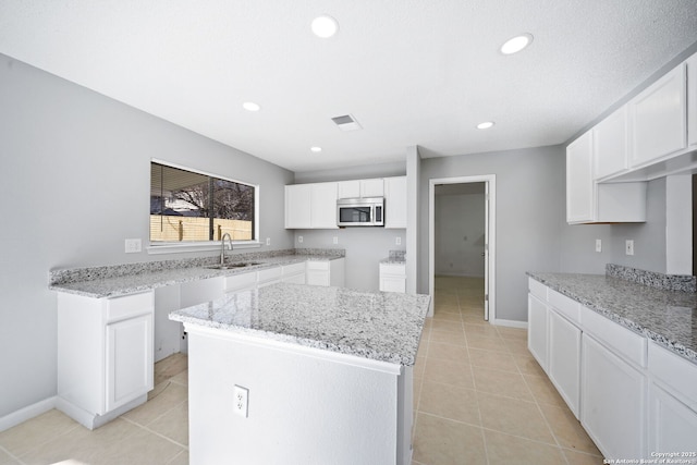 kitchen with white cabinets, a kitchen island, light tile patterned floors, and sink