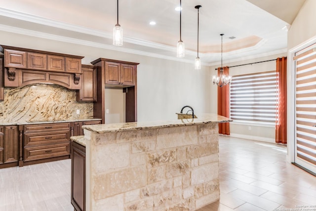 kitchen with light stone countertops, an inviting chandelier, a raised ceiling, pendant lighting, and a kitchen island with sink