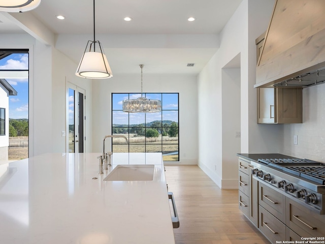 kitchen featuring custom exhaust hood, stainless steel gas cooktop, sink, pendant lighting, and light hardwood / wood-style flooring