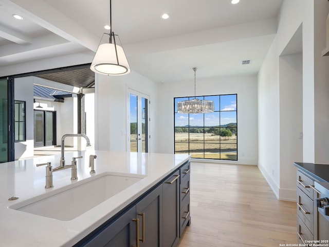 kitchen featuring sink, beam ceiling, decorative light fixtures, a notable chandelier, and light hardwood / wood-style floors