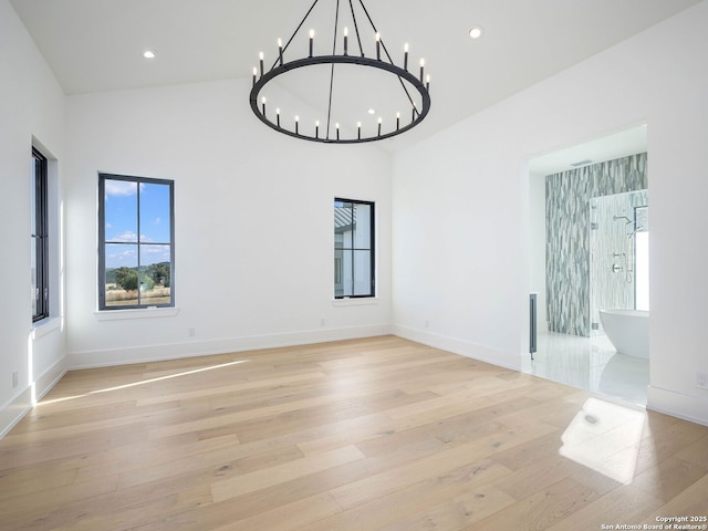 unfurnished room with a chandelier, a high ceiling, and light wood-type flooring