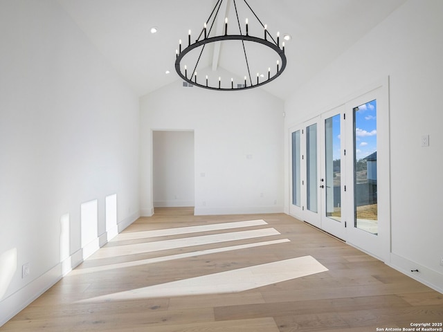 spare room featuring an inviting chandelier, light wood-type flooring, high vaulted ceiling, and french doors