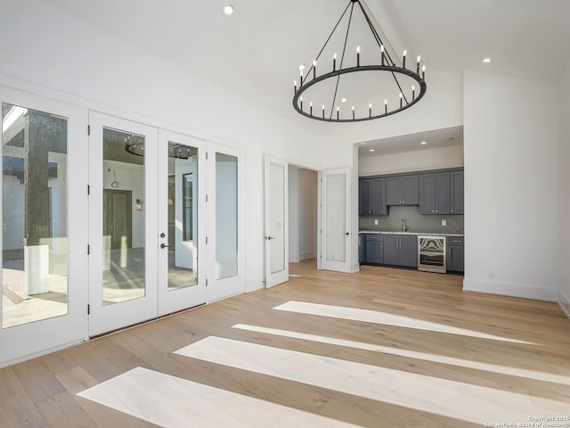 unfurnished living room with french doors, an inviting chandelier, beverage cooler, and light wood-type flooring