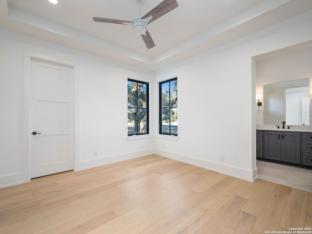 unfurnished bedroom with light hardwood / wood-style flooring, ensuite bathroom, a raised ceiling, and sink