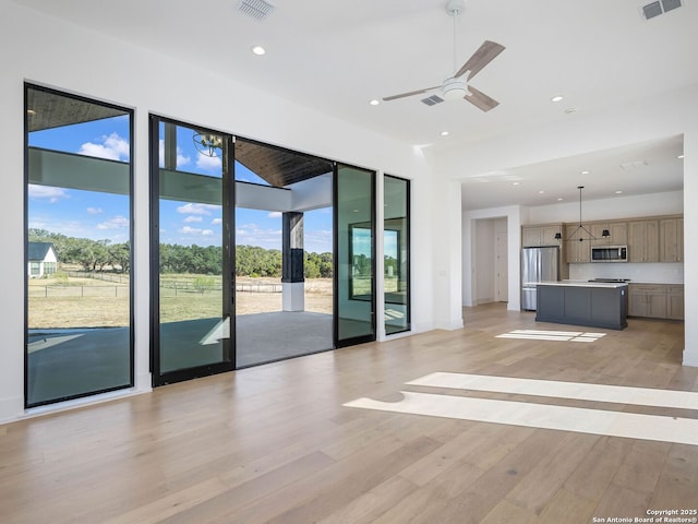 unfurnished living room featuring ceiling fan, light hardwood / wood-style flooring, and a towering ceiling